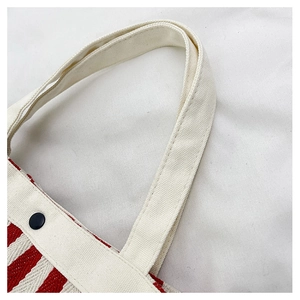 Détail du sac seau en toile à rayures rouges et blanches avec poignée et bouton noir