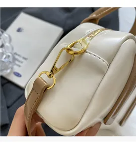 Detail of gold metal buckle and zipper on white leather handbag with brown strap