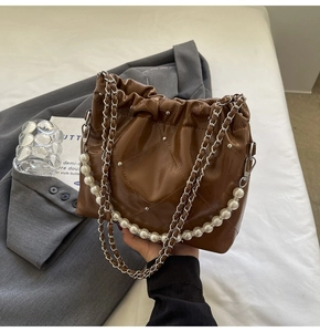 Detail of brown quilted bucket bag with silver studs, pearl handle and chain strap