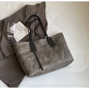 Detailed top view of a dark gray leather tote bag with embossed lettering on a brown blazer