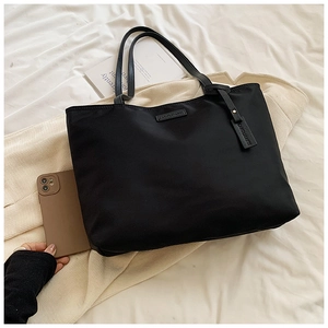 Top view of large black oxford tote bag with Carolmarti logo on a white bed