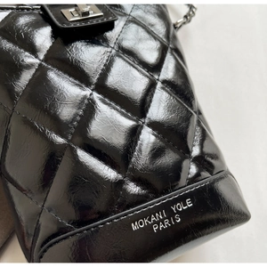 Close-up of quilted black leather bucket bag with silver logo and glossy finish