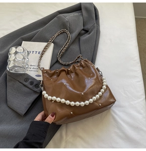 Detail of caramel quilted bucket bag with pearl handle and metallic chain strap texture