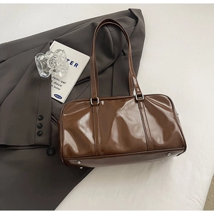 Detail of a brown patent leather tote with silver metal rings and protective feet