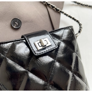 Detail of silver rectangular turn-lock on black quilted chain bucket bag with glossy finish