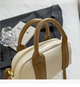 Detail of cream white Boston bag with brown handles and durable golden metal zippers