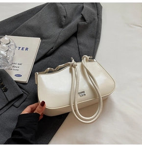Detail of a creamy white glossy leather handbag featuring a wavy metal top handle