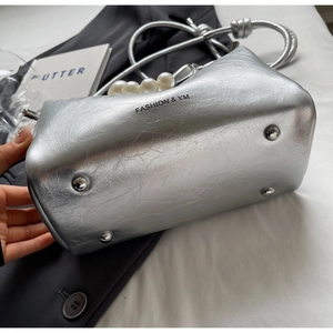 Detailaufnahme einer silbernen Handtasche mit Perlengriff und Metallfüßen am Taschenboden
