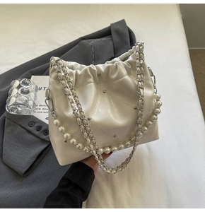 Close-up of beige quilted bucket bag featuring pearl handle and metal stud details