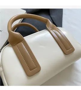 Close-up of cream faux leather Boston bag with brown handles and detailed stitching