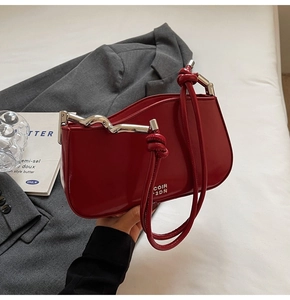Detail of red patent leather handbag with wavy silver metal rod and knotted strap detail
