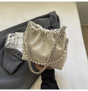 Detail of creamy white pleated bucket bag featuring pearl handle and metallic rivets