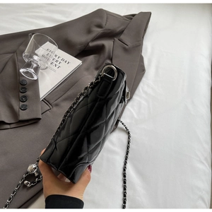 Detail of black patent leather bucket bag with silver chain and ball pendant on grey suit