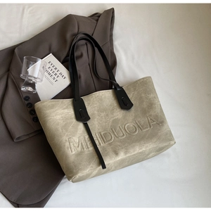 Detailed texture of olive tote bag featuring embossed MEIDUOLA letters and thin black straps