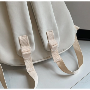 Detail of padded shoulder straps and adjustable buckles on a cream canvas backpack
