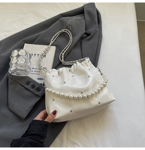 Detail of white quilted cloud bag featuring faux pearl chain and metallic rivets