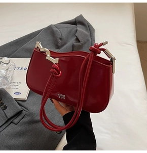 Close-up of burgundy glossy leather handbag with silver wavy metal hardware and logo