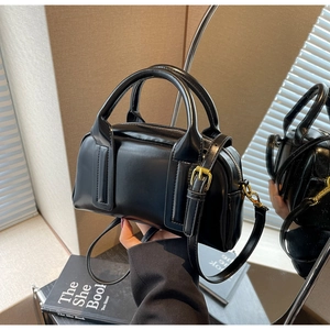 Detail shot of a black glossy Boston handbag with gold buckle and adjustable strap