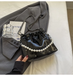 Detail of black quilted bucket bag with pearl handle and silver rivet studs on suit