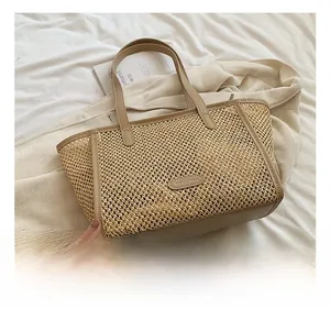 Détail d'un grand sac cabas en paille tissée avec anses en cuir beige sur fond épuré