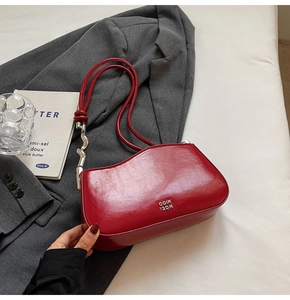 Detail of red asymmetrical shoulder bag with silver hardware on a gray background