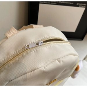 Close-up of dual-zipper closure on beige canvas backpack with woven top handle detail