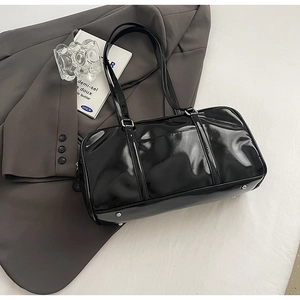 Close-up of glossy black patent leather shoulder bag on a dark gray blazer suit