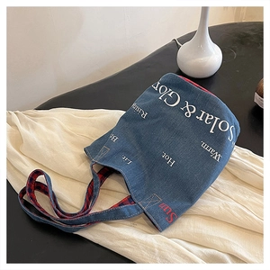 Vista dettagliata della borsa in denim con scritte artistiche e tracolla a quadri rossi