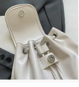 Close-up of off-white glossy leather bucket bag with silver magnetic snap and drawstring