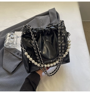 Detail of black quilted bucket bag with silver studs and elegant pearl handle strap