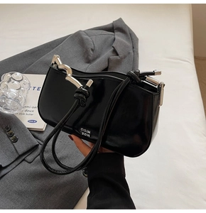 Detail of glossy black leather underarm bag featuring wavy silver metal hardware