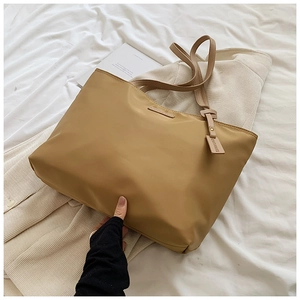 Detail view of large beige oxford tote bag with CAGLIARI metal plate on white linens