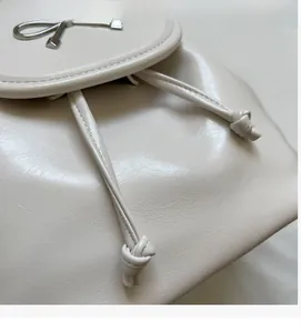 Close-up of cream faux leather backpack with silver bow buckle and drawstring