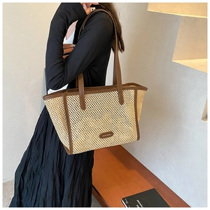 Détail d'un sac cabas en paille avec anses en cuir marron et logo en cuir cousu