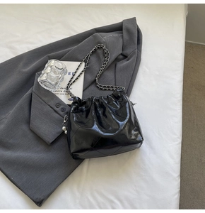 Detail of black glossy quilted bucket bag with pearl charm and chain strap on grey blazer