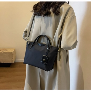 Close-up of black nylon tote bag with leather trim worn with a beige trench coat
