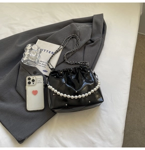 Quilted black bucket bag with pearl handle and silver studs on a gray blazer