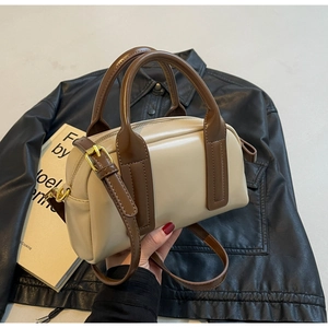 Close-up of cream Boston bag with brown handles and gold hardware on a dark background