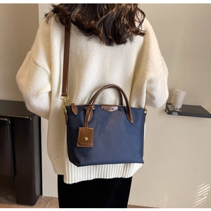 Navy blue nylon tote bag with brown leather handles worn by a model in a lifestyle scene