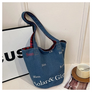 Dettaglio della borsa a secchiello in denim blu con scritte bianche e fodera a quadri rossi