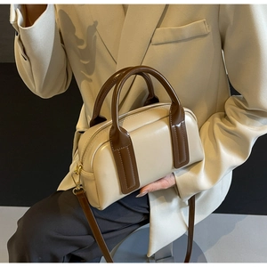 Detail of cream Boston bag with dark brown handles and golden hardware on a beige suit