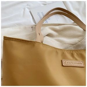 Detailed close-up of khaki oxford fabric tote bag with brand leather patch and stitching