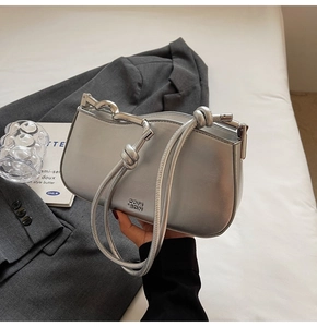 Detail of silver metallic underarm bag with knot strap and branded embossing