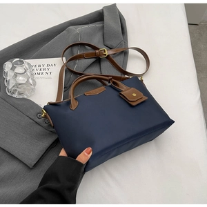 Detail of navy blue nylon tote bag with brown leather handles on a grey suit background