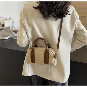 Detail of a cream Boston bag with brown straps styled on a model in a cafe setting