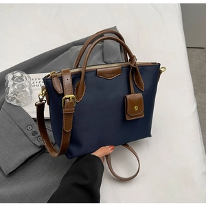 Close-up of navy nylon tote bag featuring brown leather trim and a small square pendant