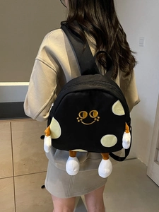 Black cartoon canvas backpack with smiling face embroidery and plush limbs on model