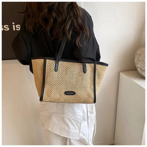 Détail d'un cabas en paille tressée avec lanières en cuir noir et logo en cuir HOCOMU