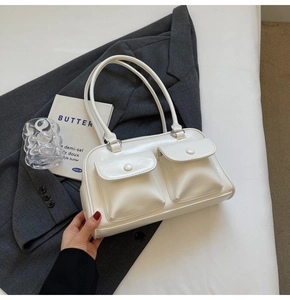 Détail du sac à bandoulière blanc crème avec deux poches frontales sur une veste grise