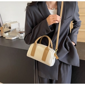 Detail of a white and khaki Boston bag with gold-tone hardware on a model with a blazer